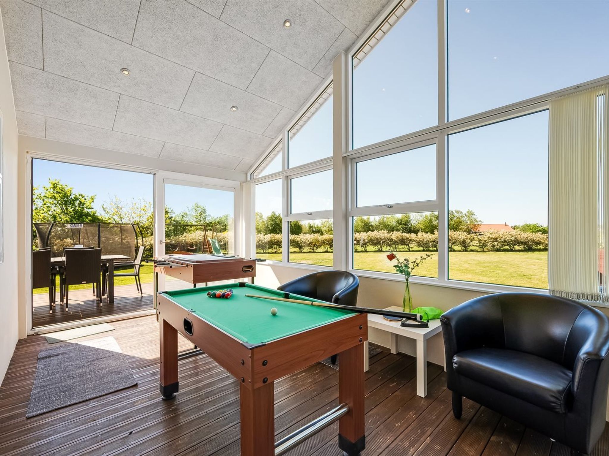 A pool table in a room with large windows, a pool table, a pool cue, a pool table chair, and a sofa.