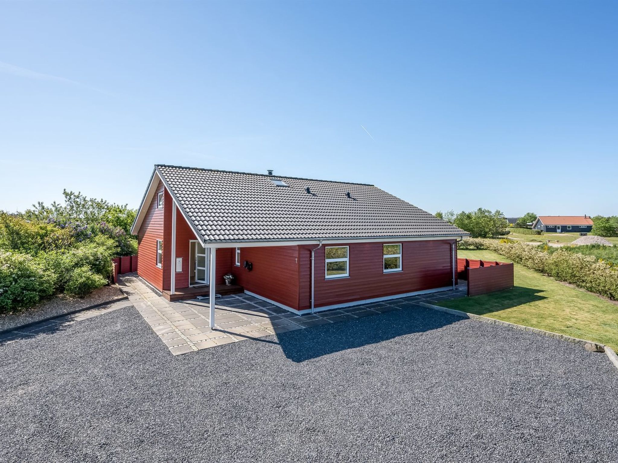 A red single-story house with a tiled roof, a covered porch, and a gravel driveway.