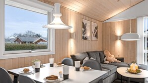 Una sala de estar moderna con comedor, paredes de madera y ventanas grandes.