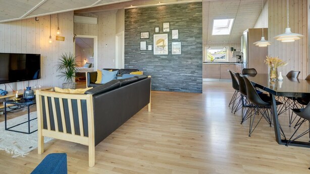 A spacious living area with a large sofa, dining table, and chairs, wooden floors, and a stone accent wall. - "Eicke" - 12km from the sea by Interhome (Oksbøl)