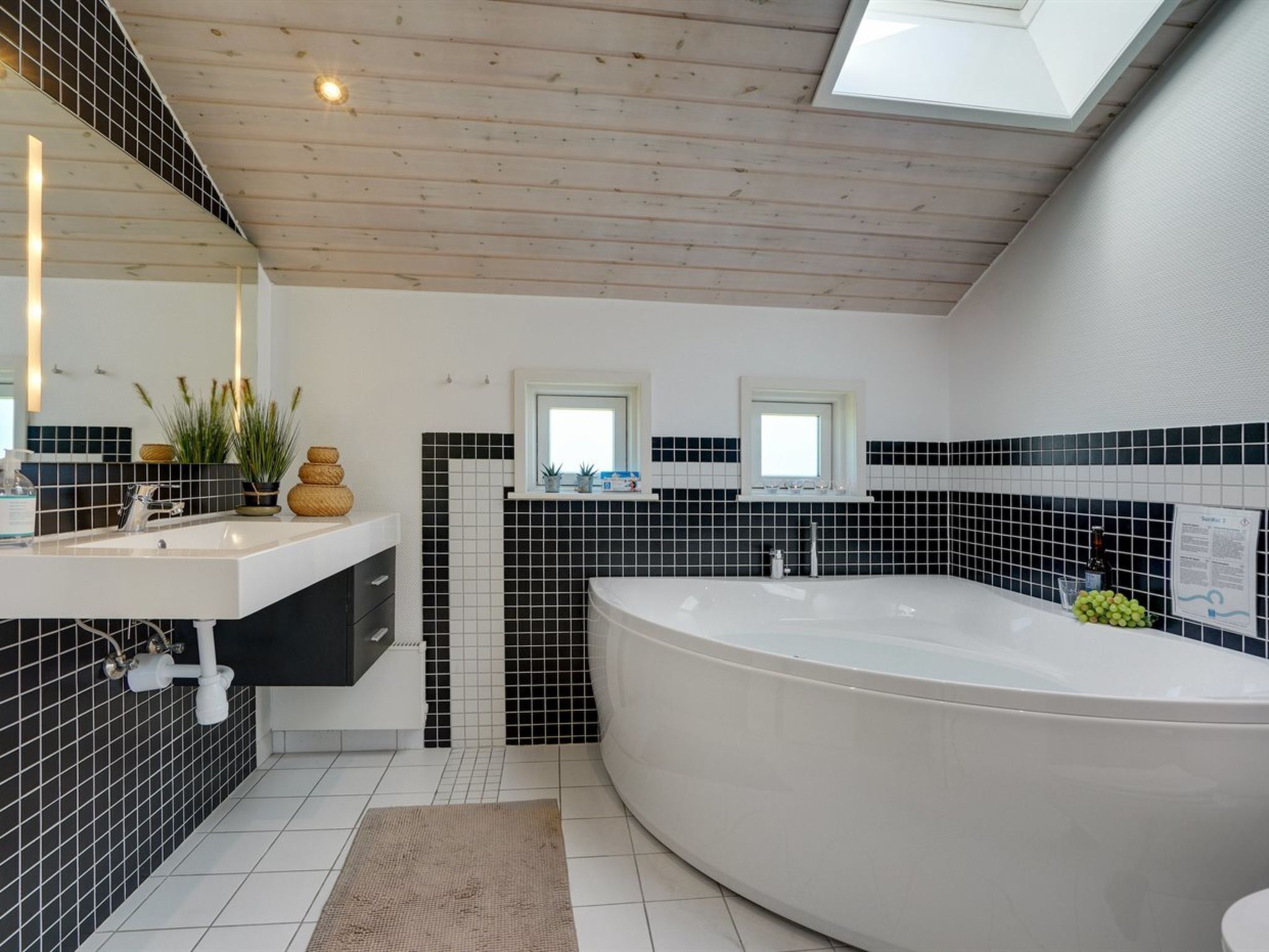 A modern bathroom with a freestanding bathtub, a large mirror, and a black and white tiled backsplash.