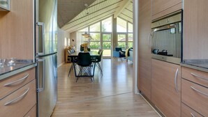 A modern kitchen with wooden cabinets, a dining area with a table and chairs, and large windows allowing natural light. - "Eicke" - 12km from the sea by Interhome (Oksbøl)