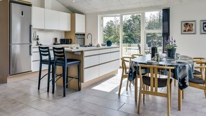 Une cuisine moderne dotée d’un îlot central, d’un coin repas avec une table ronde et d’une vue sur l’extérieur.