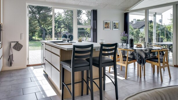Une cuisine moderne dotée d’un îlot central, de grandes fenêtres et d’un coin repas avec des chaises en bois.