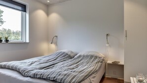 Une chambre à coucher moderne avec un lit, des lampes de chevet, une fenêtre avec des plantes et une petite table sur laquelle est posée une bougie.