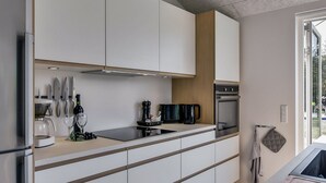 Une cuisine moderne avec des armoires blanches, un réfrigérateur en acier inoxydable, un four encastré et une machine à café.