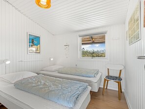Un dormitorio con dos camas, una ventana con vistas, una lámpara de pared y una pequeña mesa con una silla.