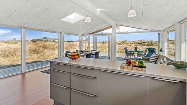 A modern kitchen with a large island, pendant lighting, and a view of the beach.