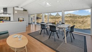 A modern kitchen with a central island, a dining area with a view of dunes, and a cozy seating area with a round table.