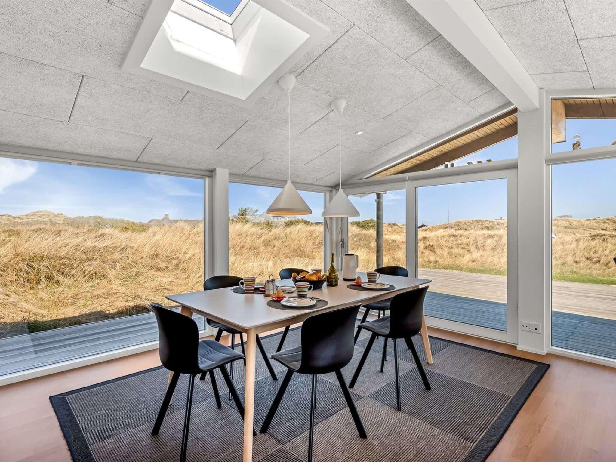Un espace repas moderne avec une grande table, des chaises noires et une vue sur les dunes.