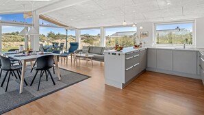 A spacious kitchen with a large island, a dining area with chairs and a table, and large windows offering views of the outdoors.