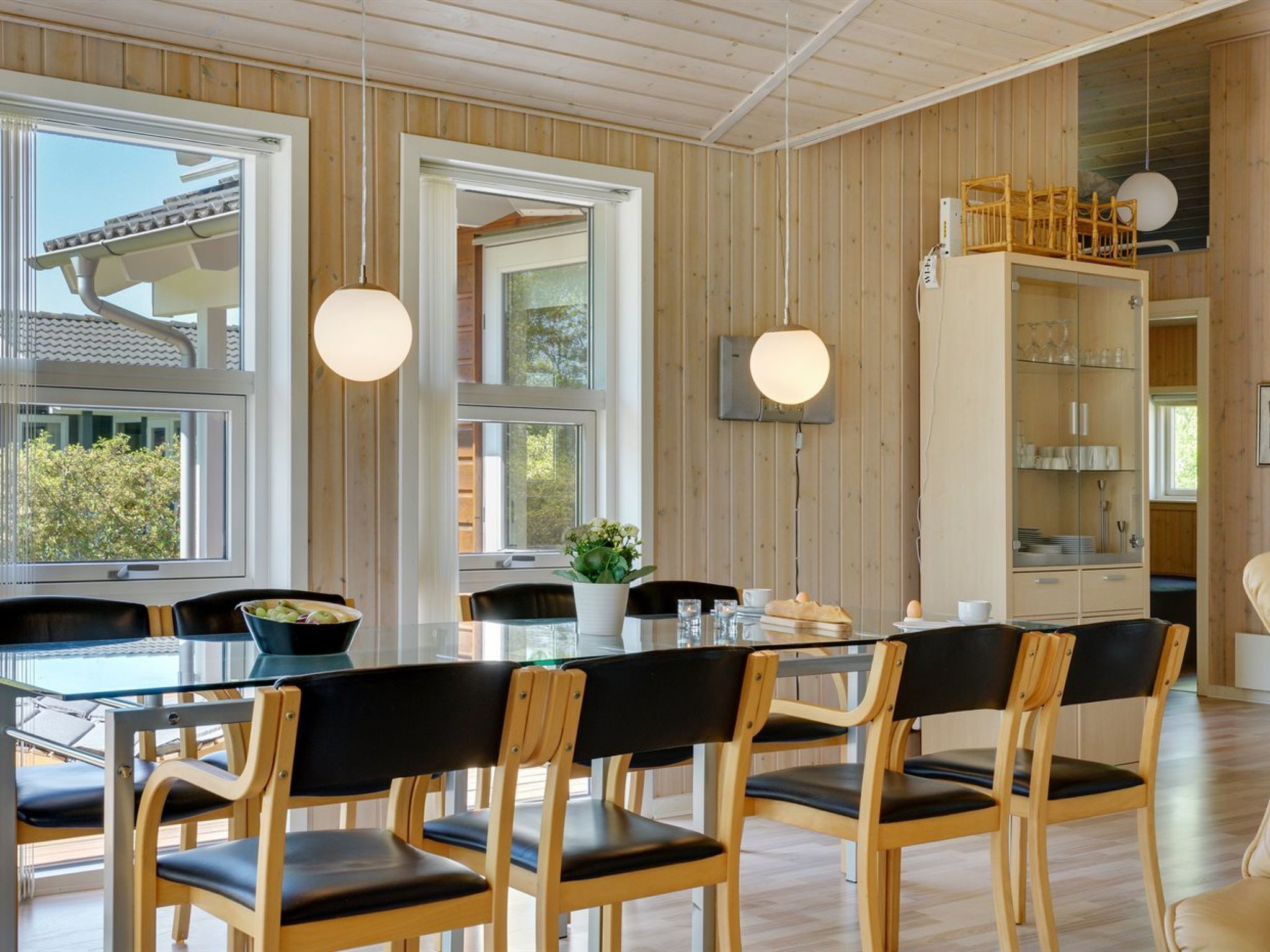 A modern dining area with a glass table, wooden chairs, and pendant lights.