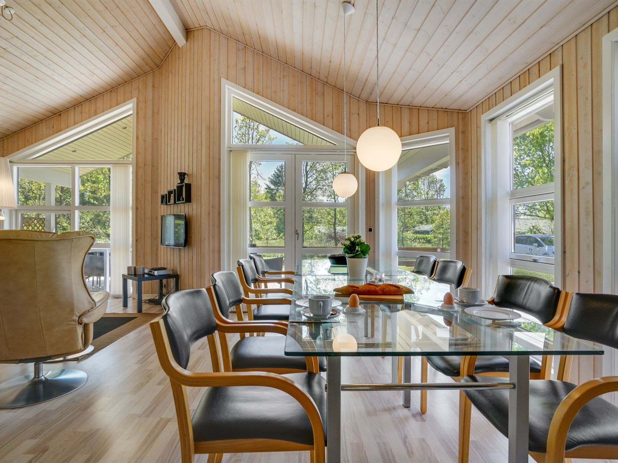 Ein stilvoller Essbereich mit einem Glastisch, Ledersesseln und Wandverkleidungen aus Holz.