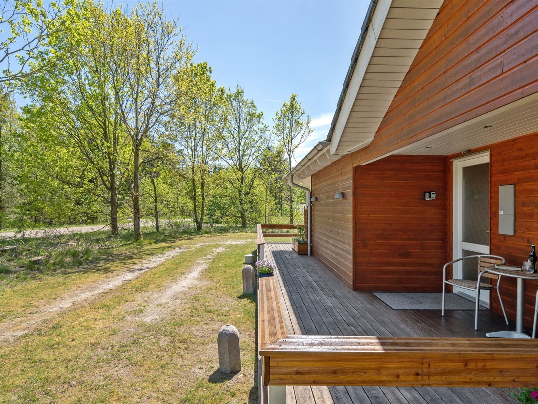 A wooden cabin with a deck, a table, and chairs, surrounded by trees.