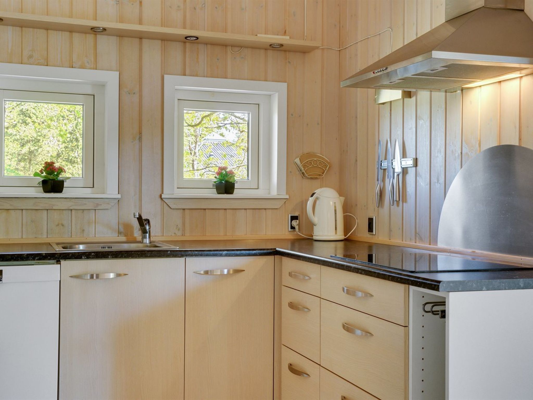 A modern kitchen with wooden cabinets, a stainless steel sink, and a kettle on the counter.