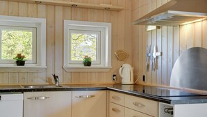 Moderni keittiö, jossa on puiset kaapit, ruostumattomasta teräksestä valmistettu pesuallas ja vedenkeitin työtasolla.