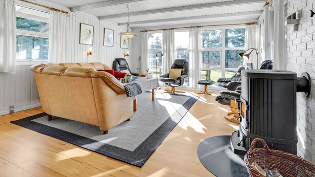 A cozy living room with a sofa, chairs, a fireplace, and large windows.