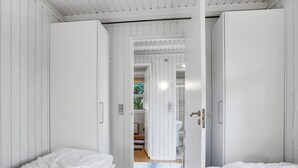 A bedroom with two beds, white walls, and a wooden floor.