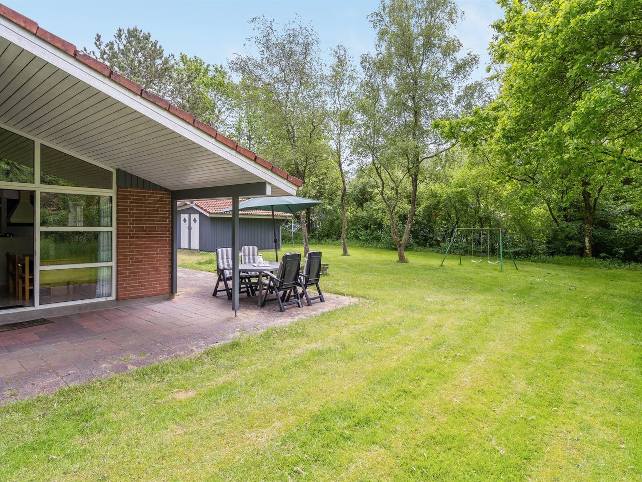 A covered patio with a table and chairs, a brick wall, and a grassy yard with trees.