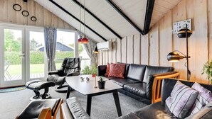 A cozy room with a black leather sofa, a wooden coffee table, and a black leather chair. There is a large window with curtains, a ceiling with exposed beams, and a wall-mounted lamp. - "Joona" - 600m from the sea by Interhome (Sydals)