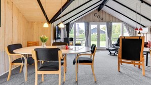 A cozy room with a wooden interior, a round table, and chairs, a fireplace, and a large window with curtains. - "Joona" - 600m from the sea by Interhome (Sydals)