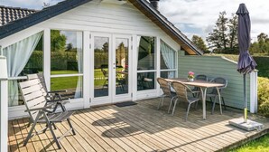 A cozy cottage with a wooden deck, a dining area with chairs and a table, and a large sliding glass door leading to a garden. - "Joona" - 600m from the sea by Interhome (Sydals)