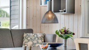 Un comedor con una mesa de madera, un tazón de ensalada, un jarrón de flores y una lámpara colgante moderna.