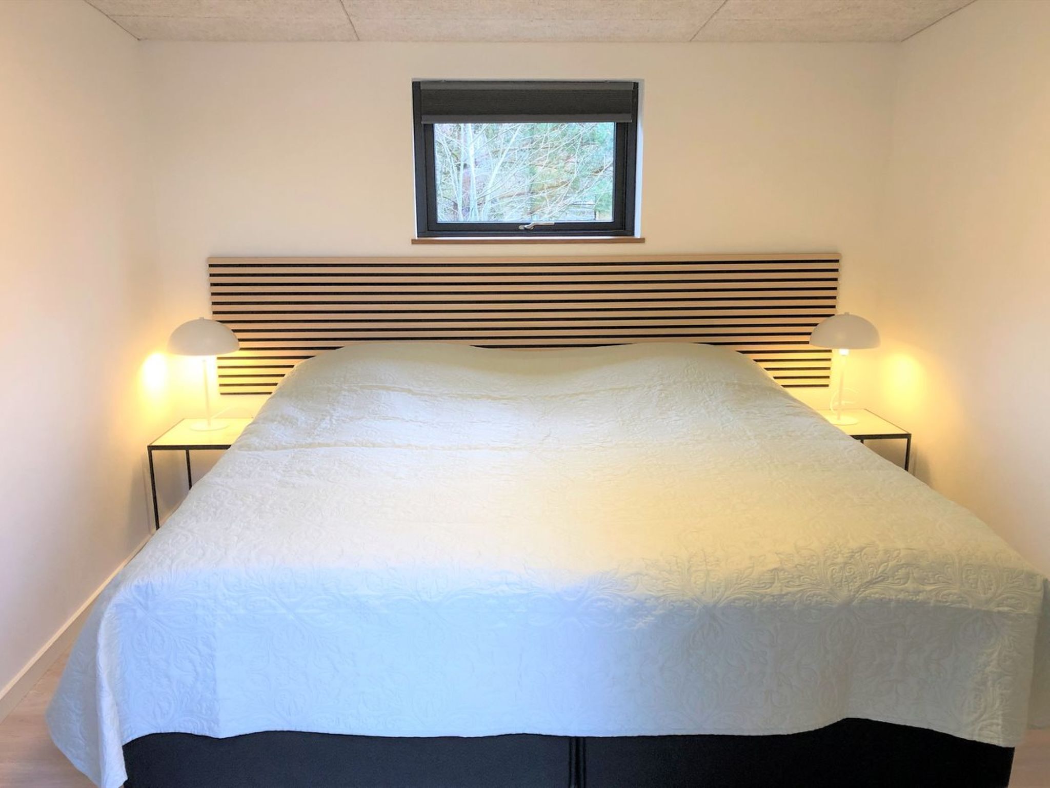 A neatly made bed with a white bedspread and a wooden headboard. There are two bedside lamps on either side of the bed.