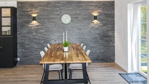A modern dining area with a wooden table, white chairs, a clock on the wall, and two wall-mounted lights. - "Rask" - 3km from the sea by Interhome (Allinge)