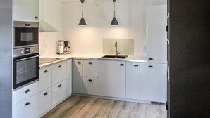 A modern kitchen with white cabinets, a built-in oven, a coffee maker, and pendant lighting. - "Rask" - 3km from the sea by Interhome (Allinge)