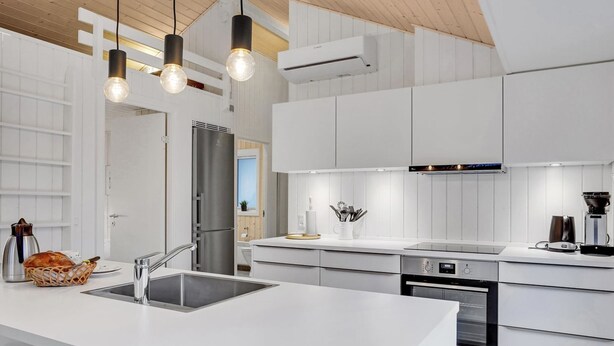A modern kitchen with white cabinetry, a stainless steel refrigerator, a built-in oven, and a coffee machine.