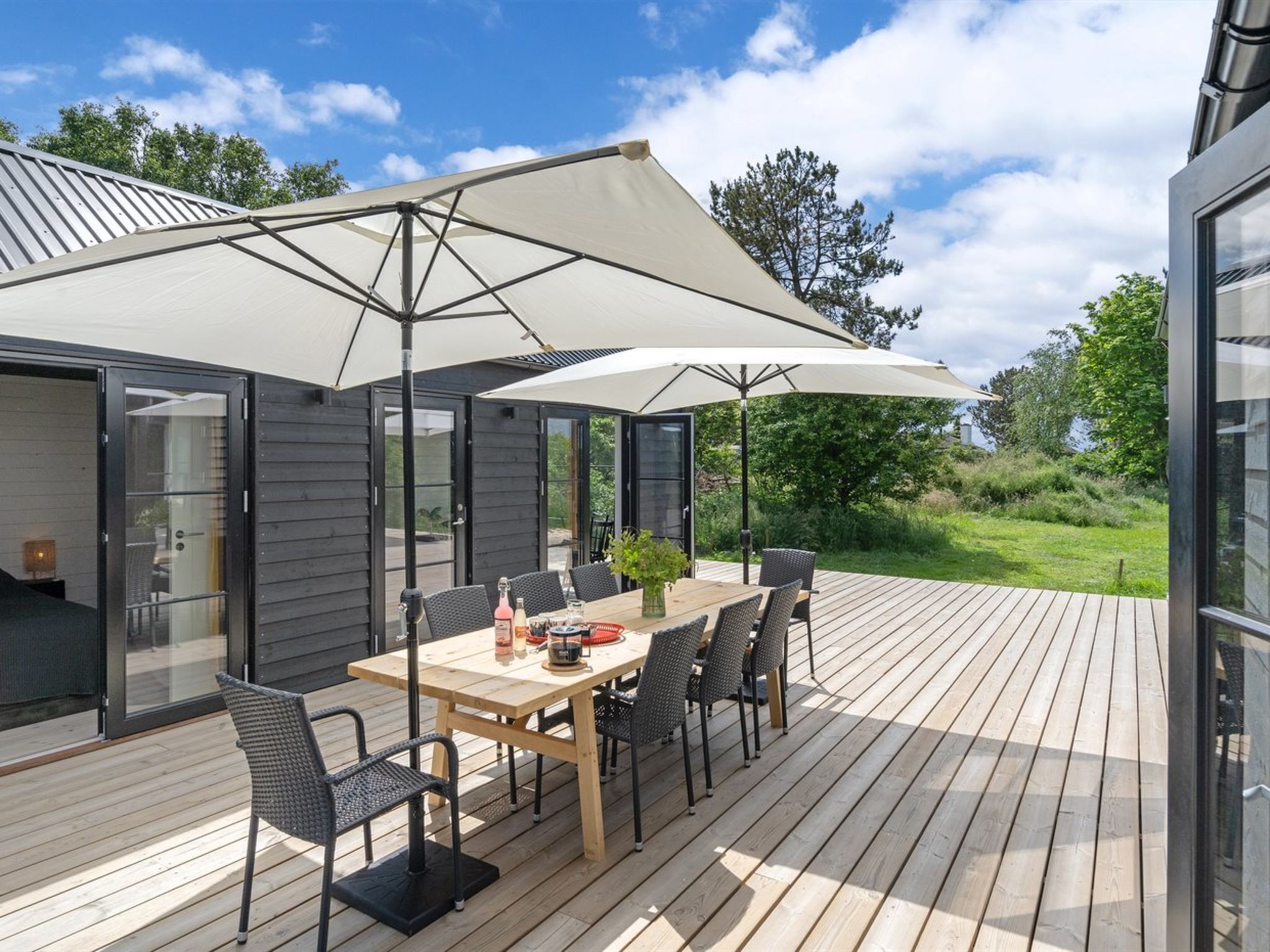 An outdoor patio with a wooden table and chairs, a large umbrella, and a glass door leading to a covered area.