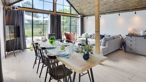 A spacious dining area with a wooden table set for four, surrounded by large windows offering a view of the outdoors.