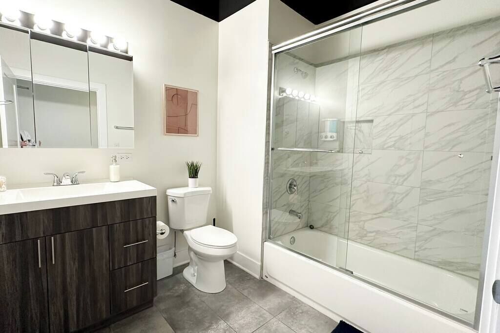 Un bagno moderno con un mobile bagno in legno scuro, accessori bianchi, una cabina doccia in vetro e piastrelle in marmo.