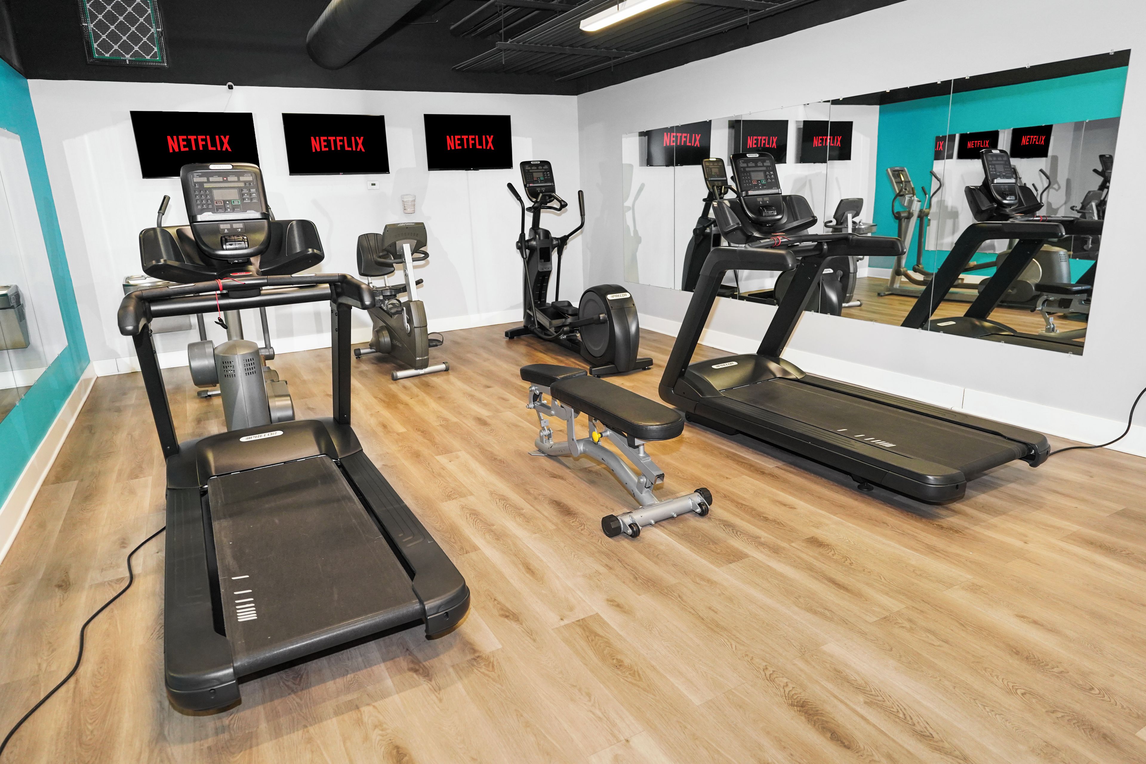 A gym with treadmills, elliptical machines, and a bench.