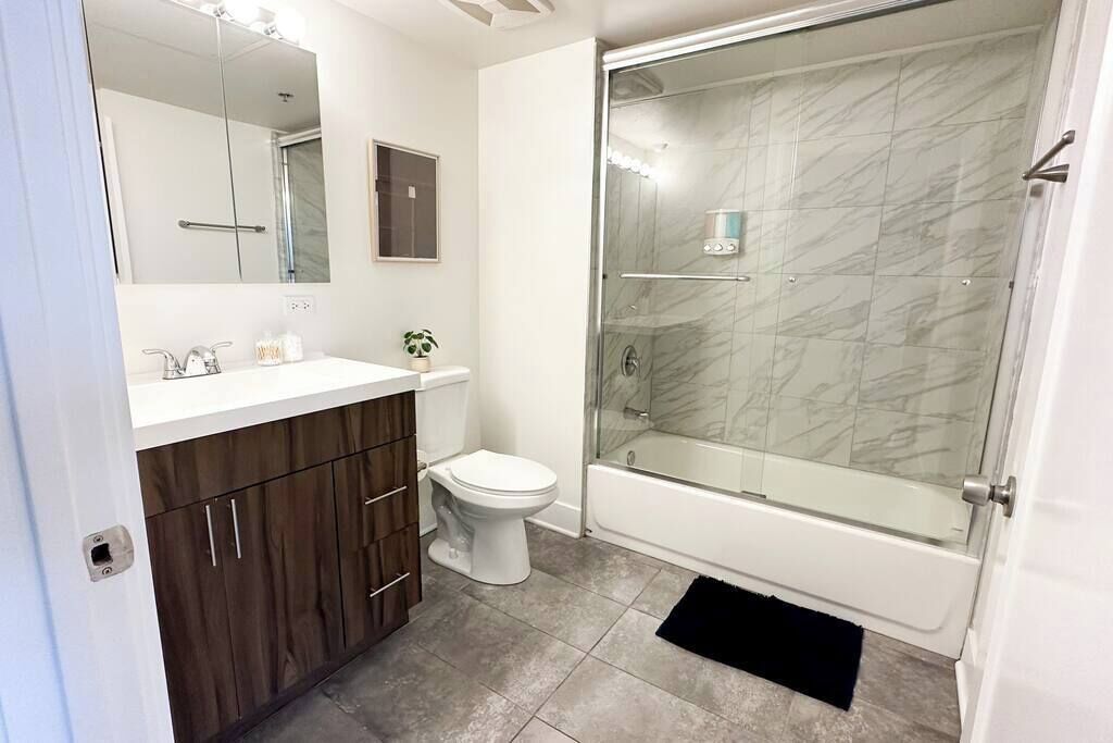 A modern bathroom with a glass-enclosed shower, a white toilet, and a vanity with a mirror and cabinets.