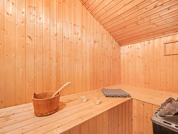A wooden sauna room with a bench, a bucket, and a glass of water.