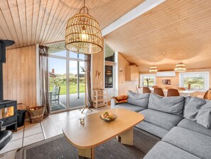 A modern interior with a wooden ceiling, a sofa, a dining table, and a large window offering a view of the outdoors.