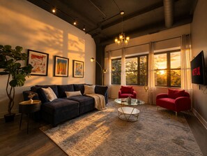 A modern living room with a dark sofa, red chairs, a glass coffee table, and a large window with curtains. - Spacious 3BR Suite South Loop Chicago Near McCormick Place & Soldier Field (Chicago)