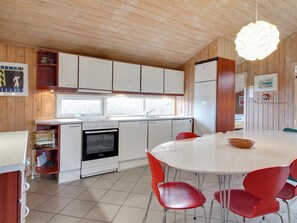 A modern kitchen with white cabinets, a built-in oven, and a dining area with a round table and red chairs.