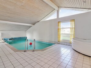 A modern indoor swimming pool with a jacuzzi, tiled flooring, and a sloped ceiling.