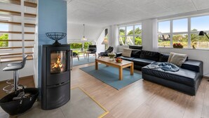 A modern living room with a fireplace, a black leather sofa, a wooden coffee table, and a view of the outdoors through large windows. - "Vangel" - 500m from the sea by Interhome (Blåvand)