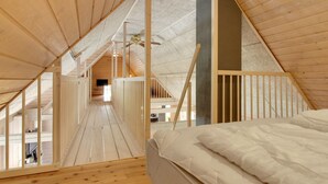 A high-ceilinged attic bedroom with wooden beams, a sloped ceiling, and a bed with white bedding.