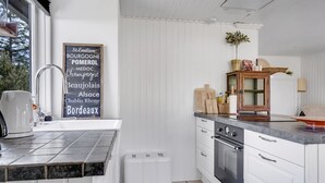 A modern kitchen with white cabinetry, a built-in oven, and a stainless steel range hood. A chalkboard sign with French wine names hangs on the wall, and a small window provides natural light. - "Noralee" - 3.5km from the sea by Interhome (Blokhus)