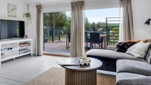 A modern living room with a flat-screen TV, a sofa, a coffee table, and a view of an outdoor deck with outdoor furniture. - "Noralee" - 3.5km from the sea by Interhome (Blokhus)
