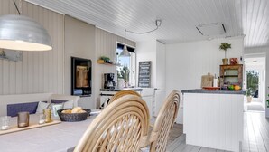 A modern kitchen with white cabinetry, a dining area with wicker chairs, and a bar area with a white countertop. - "Noralee" - 3.5km from the sea by Interhome (Blokhus)