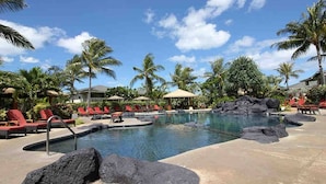 A pool area with red lounge chairs, palm trees, and a clear blue sky. - Dream of Aloha (Kapolei)