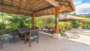 A covered outdoor seating area with a table and chairs, surrounded by lush greenery and a thatched roof structure. - Dream of Aloha (Kapolei)