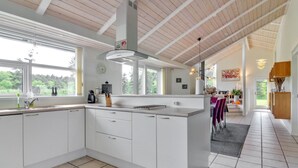 A modern kitchen with white cabinetry, a large island, and a view of the outdoors through large windows. - "Villads" - 1km from the sea by Interhome (Løkken)