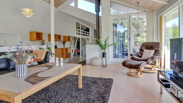 A spacious living room with a high ceiling, wooden beams, a large window, a leather armchair, a TV, and a dining area with a wooden table and chairs. - "Villads" - 1km from the sea by Interhome (Løkken)